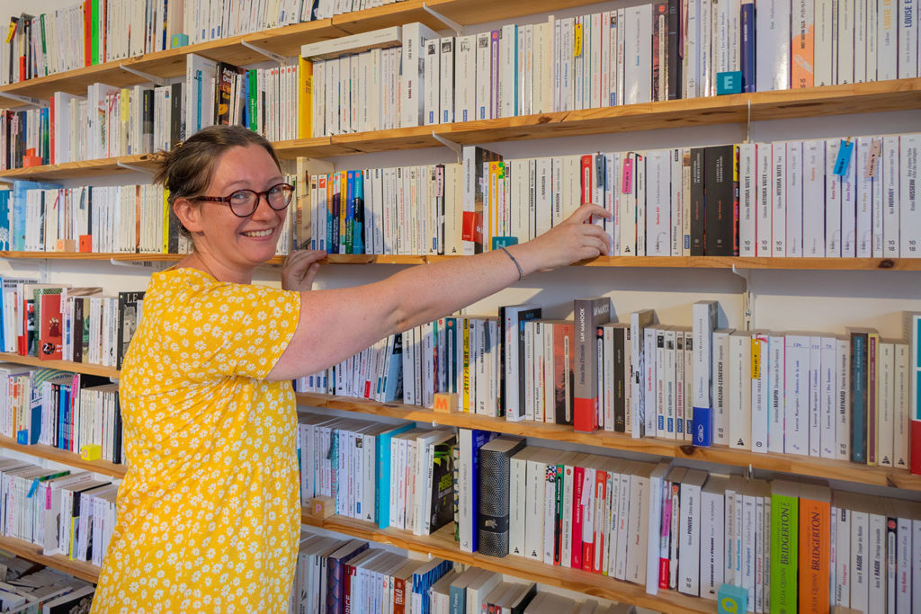 Emily, gérante de la librairie Les Lisières, range un libre dans une étagère. Elle sourit.